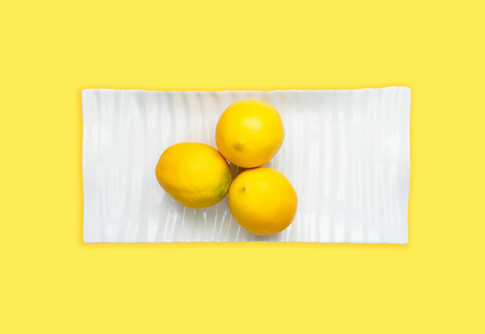 Hand holding a fresh lemon against a soft pink background